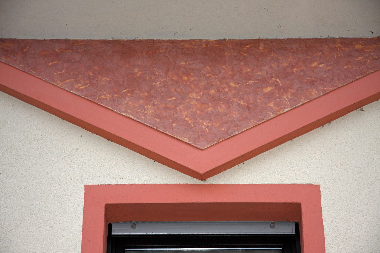 Dreieckiges Putzfeld in Terrakotta über einem Fenster